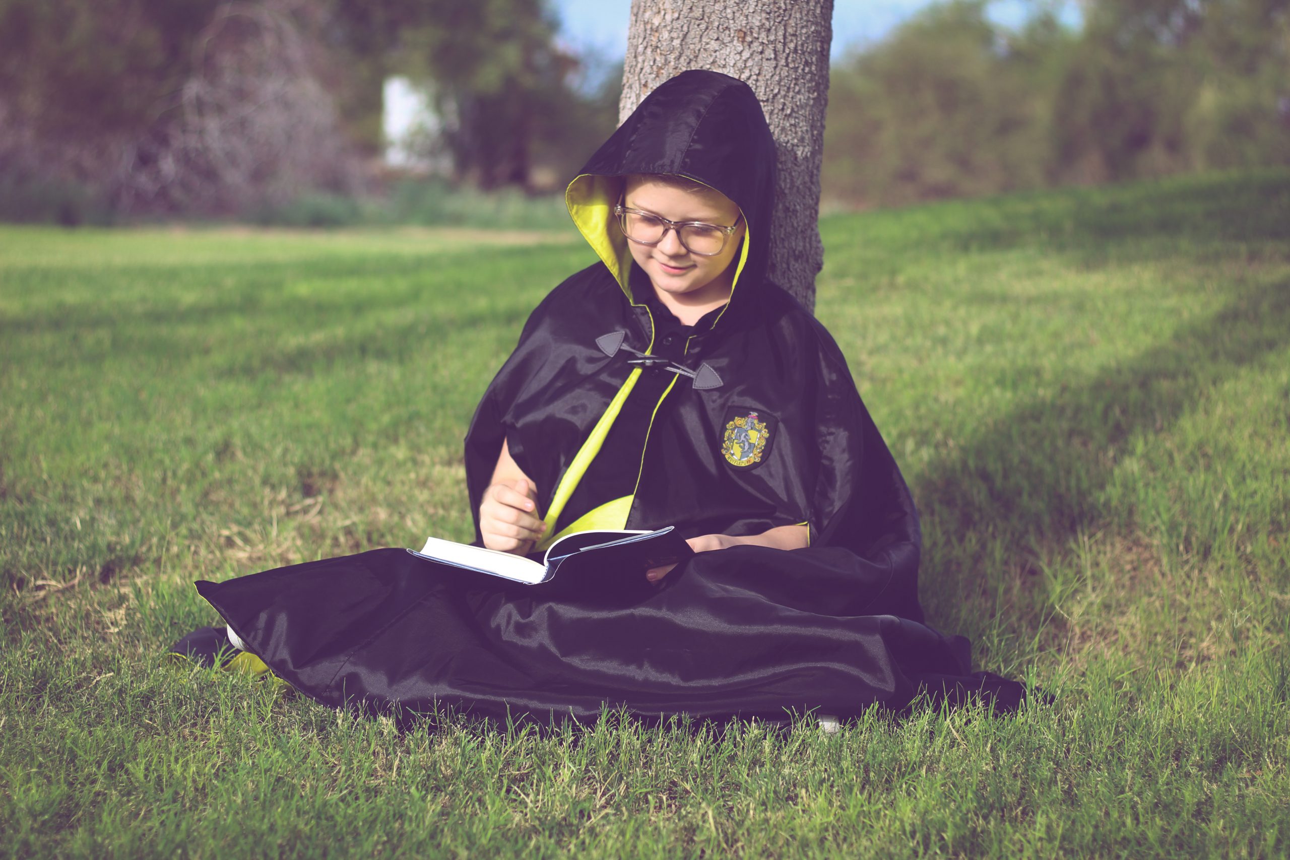 Waves and Wild Storybook Cape boy wearing Hufflepuff robe studying under a tree