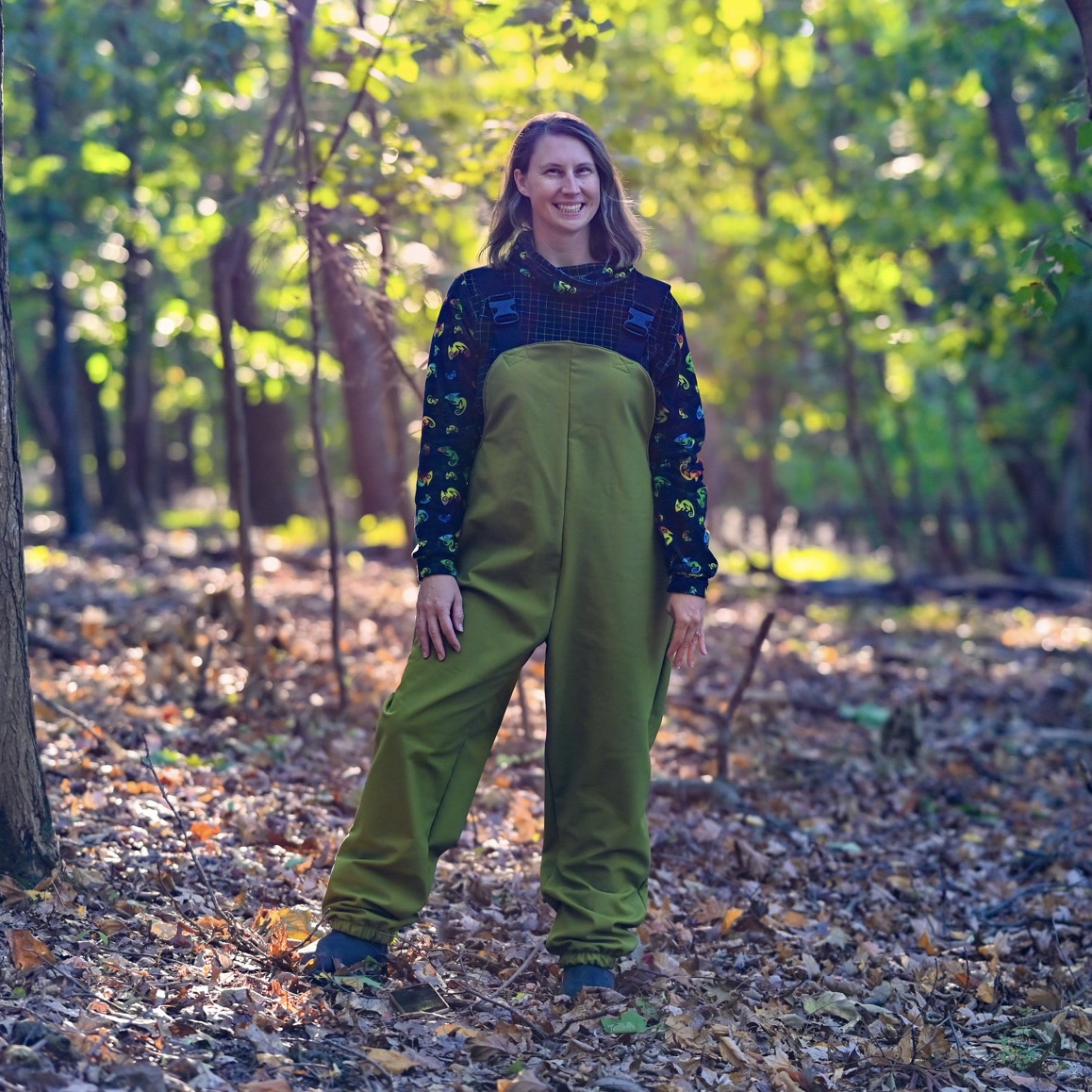Smiling person wearing green waterproof dungarees made from the Free Range Fun Over Trousers pattern.